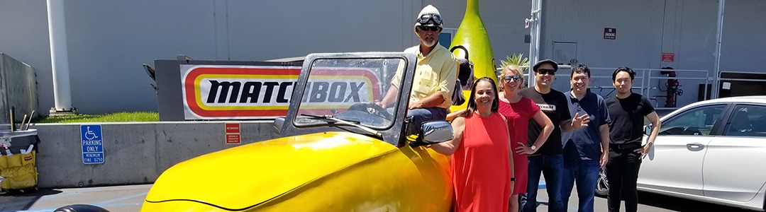 A photograph of the Big Banana Car at the Matchbox head quarters in El Segundo California. Next to the car is the team who worked on the Mattel Matchbox toy banana car.