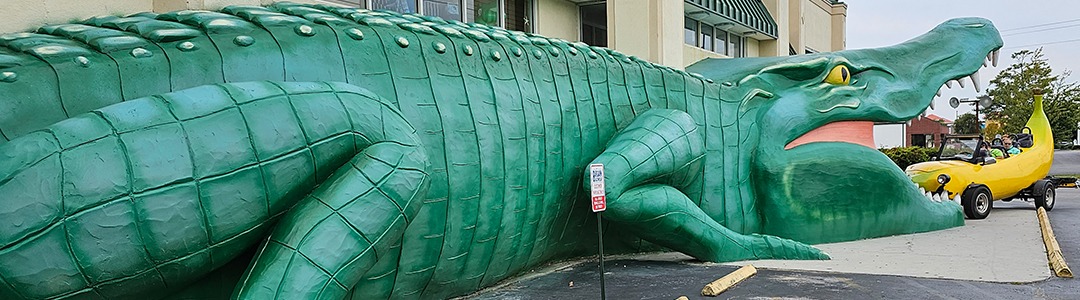 A photograph of the banana car in the mouth of an enormous alligator sculpture.